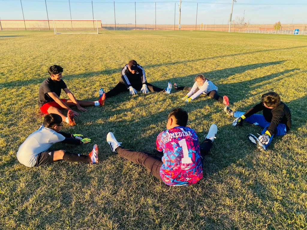 A coach and boys soccer players stretching on a field