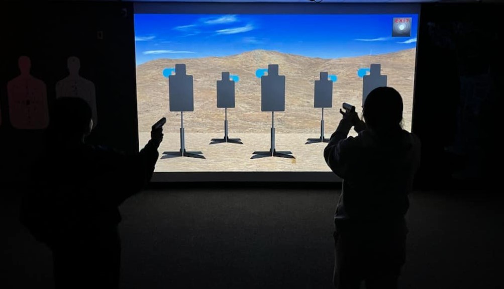 Two people play a shooting simulation game with a projector display.